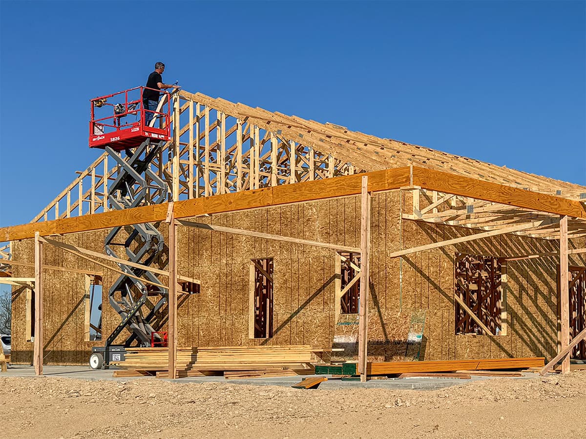 Construction worker using scissor lift to secure roof trusses