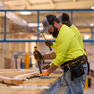 Three employees assembling a roof truss with hammers